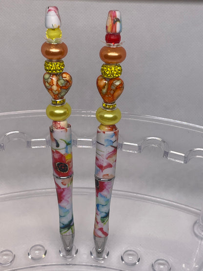 Luxury beaded pen with rose patterns and vibrant heart-shaped beads on a white background.